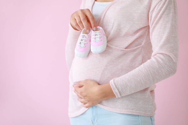 Jeune femme enceinte avec des chaussons bébé sur fond de couleur - Photo, image