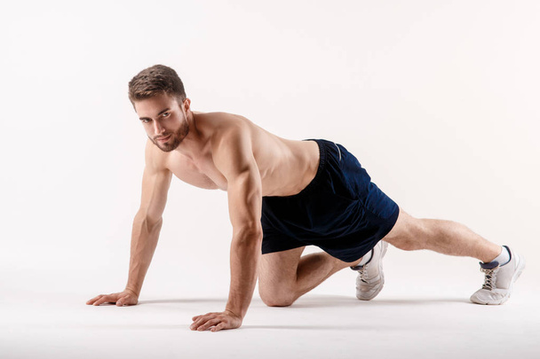 young man with a beard of a sports physique doing push-ups from the floor on a white isolated background, sportsman goes in for sports - Fotoğraf, Görsel