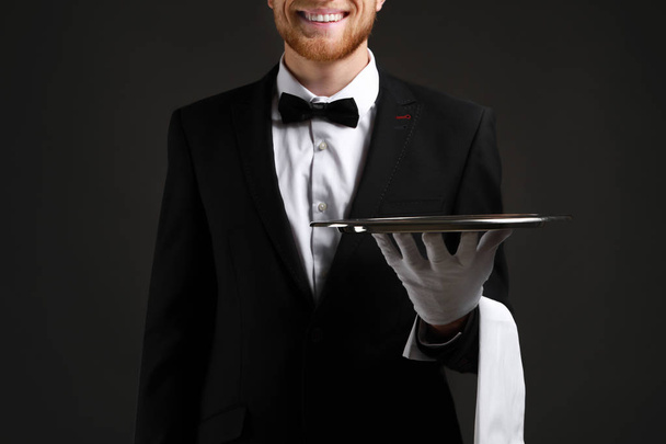 Handsome waiter with empty tray on dark background - Photo, Image