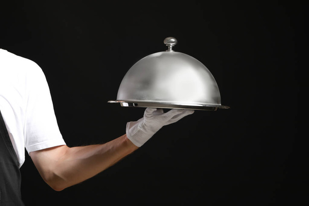 Mano de camarero con bandeja y cloche sobre fondo oscuro
 - Foto, Imagen