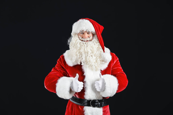 Porträt des Weihnachtsmannes mit erhobenem Daumen auf dunklem Hintergrund - Foto, Bild