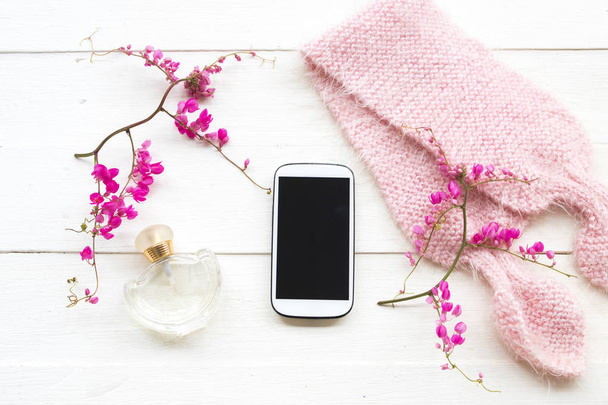 téléphone portable, parfum et rose tricot écharpe de laine de style de vie femme se détendre l'hiver avec coloré petites fleurs roses arrangement plat style laïc sur fond blanc en bois
  - Photo, image
