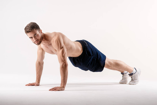 young man with a beard of a sports physique doing push-ups from the floor on a white isolated background, sportsman goes in for sports - Photo, Image