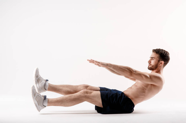 young man with a beard of a sports physique does an exercise on the muscles of the abdominal cavity on a white isolated background, the athlete goes in for sports, exercise on the muscles of the press - Φωτογραφία, εικόνα