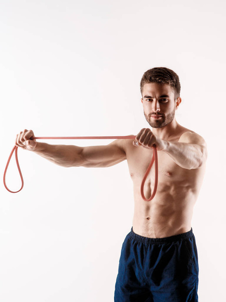 Young sporty man with a beard on a white background with gymnastic elastic bands in his hands. training with rubber bands - Foto, Bild