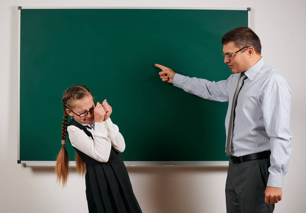 怒っている教師は女子高生に叫び、黒板の背景でポーズをとる - 学校と教育の概念に戻る - 写真・画像