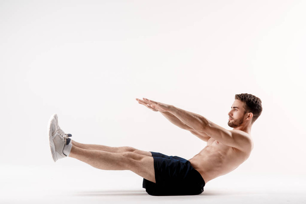 young man with a beard of a sports physique does an exercise on the muscles of the abdominal cavity on a white isolated background, the athlete goes in for sports, exercise on the muscles of the press - Photo, Image