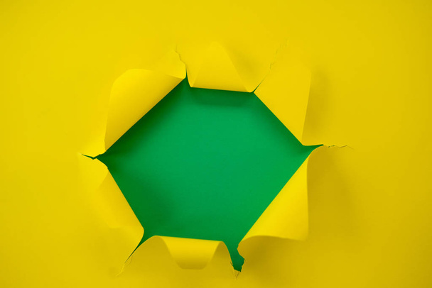ripped yellow paper against a green background - Φωτογραφία, εικόνα