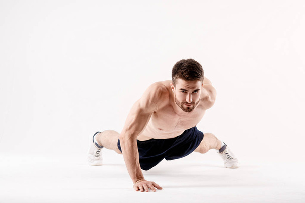 young man with a beard of a sports physique doing push-ups from the floor on a white isolated background, sportsman goes in for sports - Φωτογραφία, εικόνα