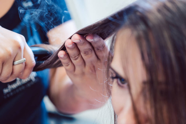 Coiffeur à l'aide de fer plat sur les cheveux de la femme client
 - Photo, image