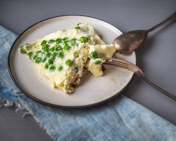 Domácí omeleta snídaně se zeleným hráškem na keramické kulaté desce s vidličkou a lžičkou, pohled shora - Fotografie, Obrázek