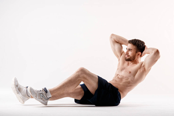 young man with a beard of a sports physique does an exercise on the muscles of the abdominal cavity on a white isolated background, the athlete goes in for sports, exercise on the muscles of the press - Zdjęcie, obraz