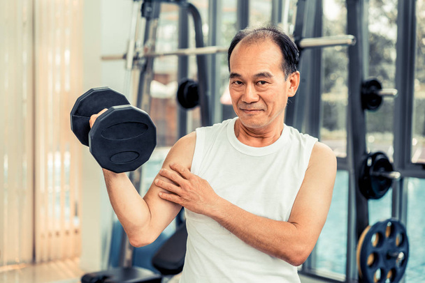 Senior man lifting dumbbell in fitness gym. - Photo, Image