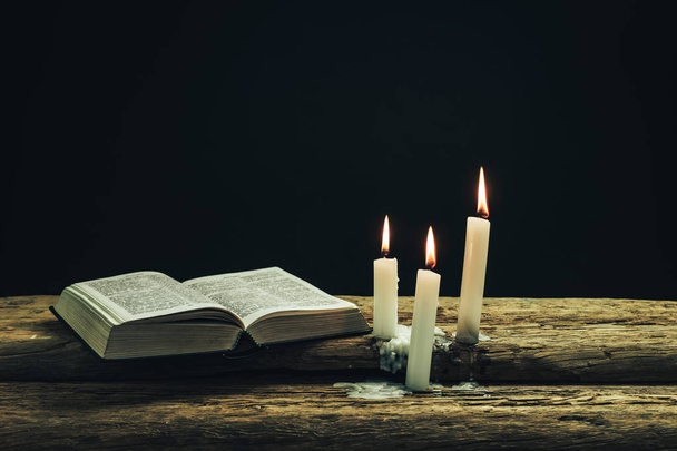 Красива відкрита Біблія і спалені свічки на старому дубовому дерев'яному столі і темному фоні
.  - Фото, зображення