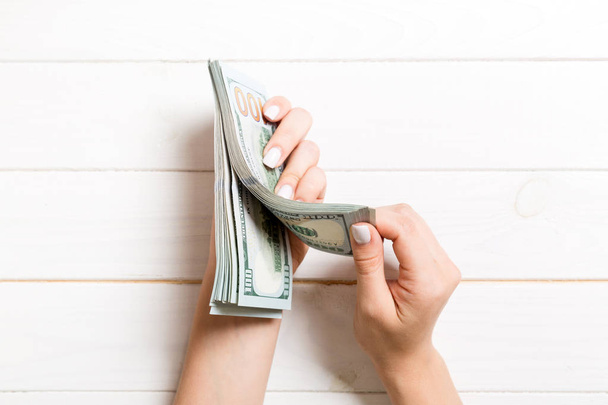 Vista superior de las manos de una mujer de negocios contando billetes de cien dólares sobre fondo de madera. Concepto de éxito y riqueza
 - Foto, imagen