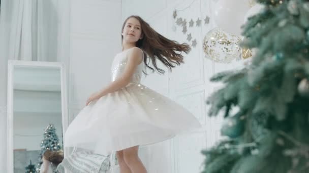 Όμορφη κορίτσι γυρίζοντας κοντά χριστουγεννιάτικο δέντρο σε λευκό φόρεμα. - Πλάνα, βίντεο
