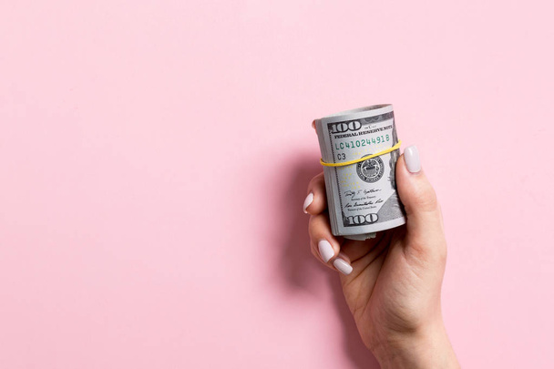 Top view of female hand holding a pack of rolled money on colorful background. One hundred dollars. Business concept with empty space for your design. Charity and tips concept - Zdjęcie, obraz