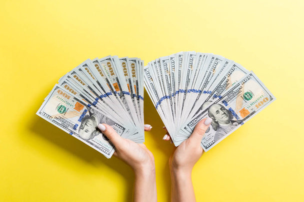 Abanico de billetes de cien dólares en manos femeninas sobre fondo colorido. Concepto de inversión
 - Foto, Imagen