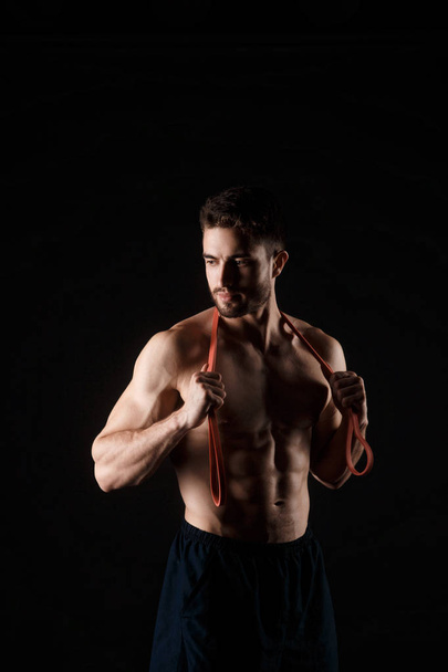 sports man with a beard on a black background with gymnastic elastic bands in hands - Фото, изображение
