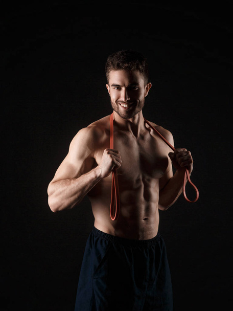 sports man with a beard on a black background with gymnastic elastic bands in hands - Fotoğraf, Görsel