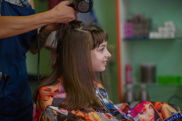 Stylist Friseur macht eine Frisur für ein nettes kleines Mädchen in einem Schönheitssalon. Friseur, Haarschnitt. - Foto, Bild