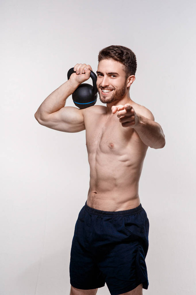 Young athlete on a white background lifts a kettlebell. training a bearded man athletic build - Valokuva, kuva