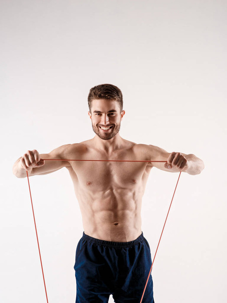 Young sporty man with a beard on a white background with gymnastic elastic bands in his hands. training with rubber bands - Foto, afbeelding