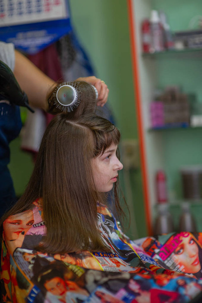 Stylist fodrász teszi a frizurát egy aranyos kislány egy szépségszalonban. Fodrászati, hajvágás. - Fotó, kép