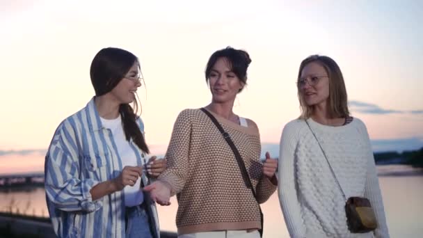 Drie mooie vrouwen wandelen en lachen bij zonsondergang. - Video