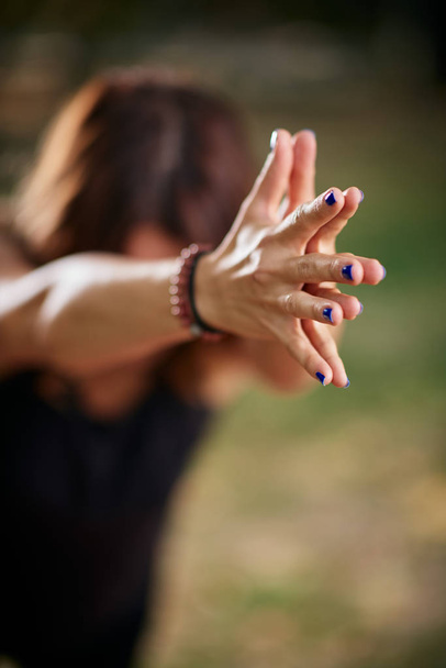 Mujer caucásica enfocada de pie en pose de yoga Guerrero III. Naturaleza exterior. Enfoque selectivo en las manos
. - Foto, imagen