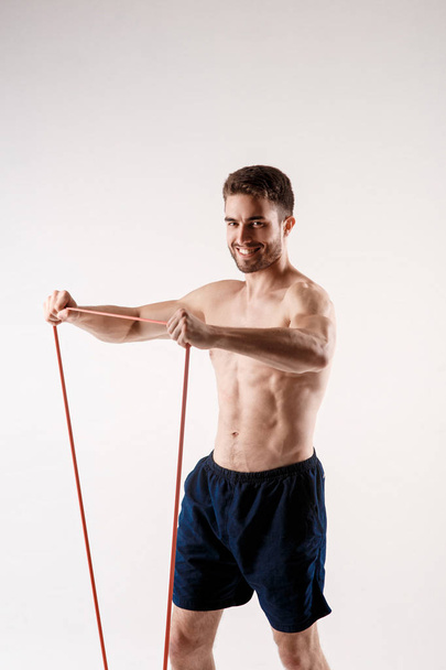 Young sporty man with a beard on a white background with gymnastic elastic bands in his hands. training with rubber bands - Foto, immagini
