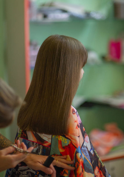 Peluquería estilista hace un peinado para una niña linda en un salón de belleza. Peluquería, corte de pelo
. - Foto, imagen