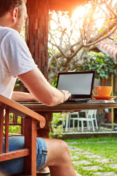 Homme avec café / thé et ordinateur portable sur un porche à la maison
. - Photo, image