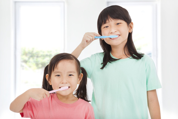 Две счастливые маленькие девочки чистят зубы
 - Фото, изображение