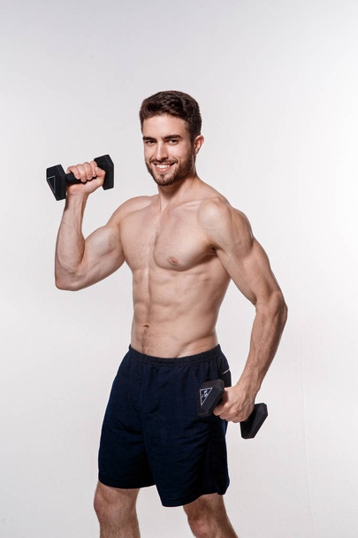Young athlete on a white background lifts dumbbells. training a bearded man athletic build - Foto, imagen