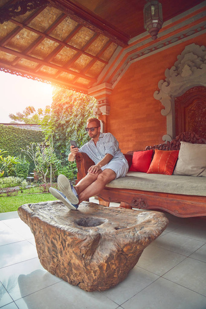 Uomo che utilizza smart phone su un divano terrazza in estate
. - Foto, immagini