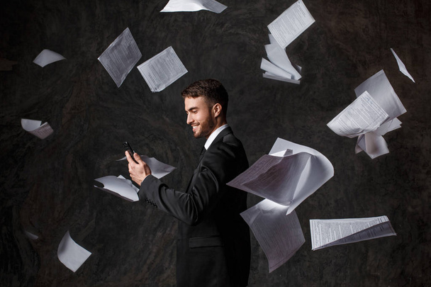 Concept of doing business through the phone. CRM systems and innovative technologies. failure to do business on paper. Young man throws a stack of documents looking at the phone screen - Foto, Imagen
