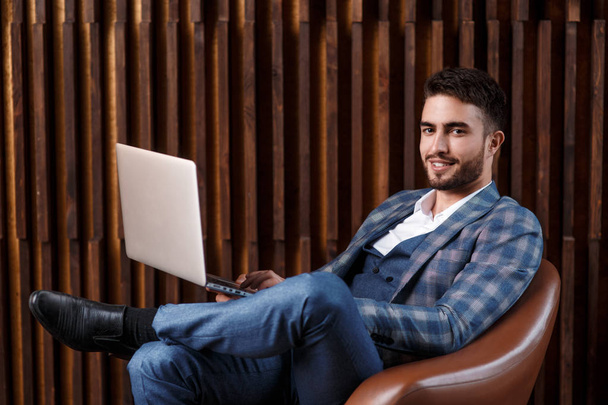 Young successful businessman is working behind a laptop while sitting in a loft office. bearded man working on a laptop - Фото, зображення