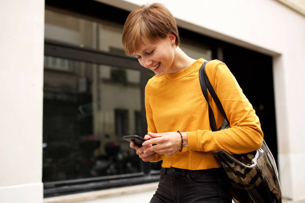 Portrait de jeune femme heureuse marchant et regardant du texte sur son téléphone portable
 - Photo, image
