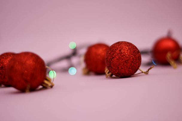 Red christmas balls with colorful lights of garland on pink background - Fotó, kép