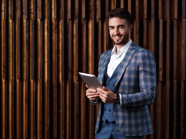 young successful businessman with a beard in a luxurious blue checked suit. Man works on a tablet in a loft office - Φωτογραφία, εικόνα