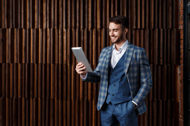 young successful businessman with a beard in a luxurious blue checked suit. Man works on a tablet in a loft office - Foto, Imagem
