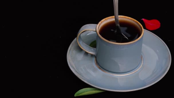 4k video Close up stir or stirring a blue coffee cup with a spoon on black background  with green leaf and red rose petal - Πλάνα, βίντεο