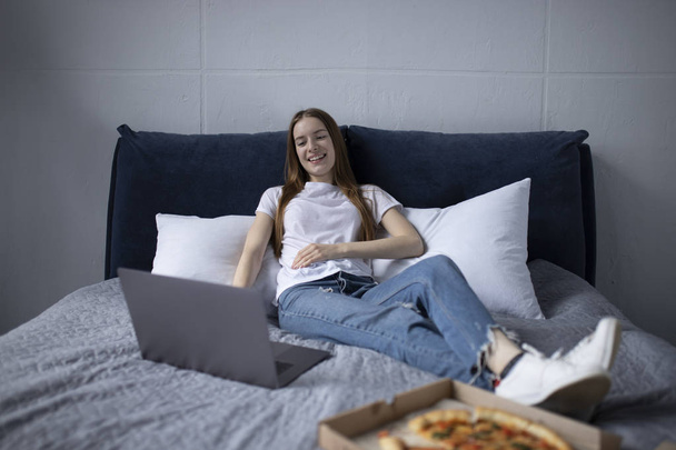 Feliz joven mujer comiendo rebanada de pizza caliente en casa y viendo
 - Foto, imagen
