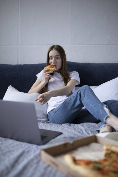 自宅でホットピザのスライスを食べて見ている幸せな若い女性 - 写真・画像