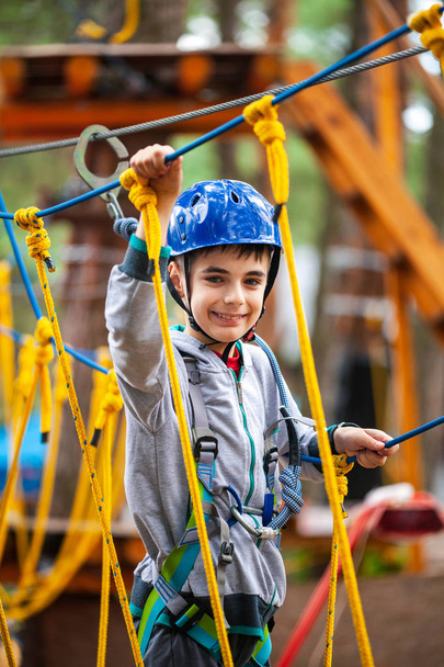 Young boy climbing pass obstacles in rope. Child in forest adventure park. - Foto, Imagen