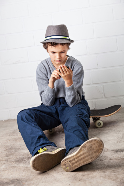 Cool Boy sitting on his skateboard, holding a smartphone - Φωτογραφία, εικόνα