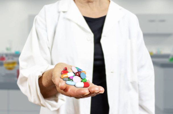 Old woman doctor holding pills, capsules, drugs and medics on a blurred laboratory background 3d rendering. Medicine, health care, overmedication and disease healing concept. - 写真・画像