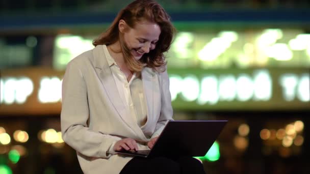 Счастливая женщина с волнением смотрит на экран ноутбука снаружи вечером
. - Кадры, видео