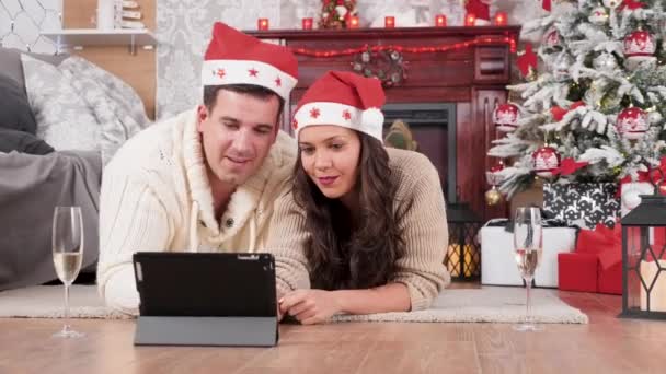 Couple lying on the floor in Christmas eve shopping online using a tablet PC - Materiał filmowy, wideo